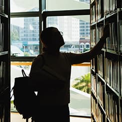Person backlit in a library picking out a book