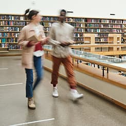 Two people walking in a library, their bodies are blurred
