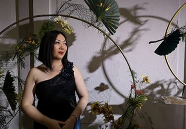 Janet in a darkened room surrounded by plants and decorations.