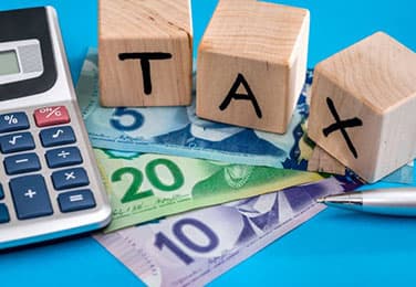 wooden blocks spelling out the word tax on top of Canadian currency and a calculator