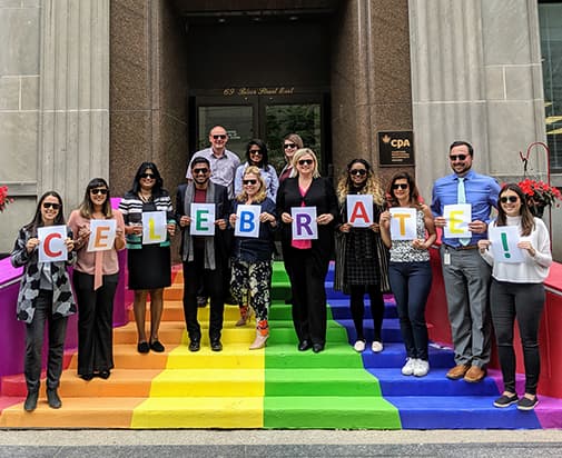 People standing on rainbow coloured stairs holding signs that spell celebrate