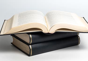 Book lying open over two other stacked books with black leather hardcover bindings