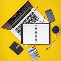 Laptop, notebook, calculator, phone, glasses and coffee on a yellow desk